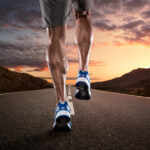 Close up of athlete's legs running on the empty road at the sunset