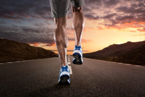 Close up of athlete's legs running on the empty road at the sunset
